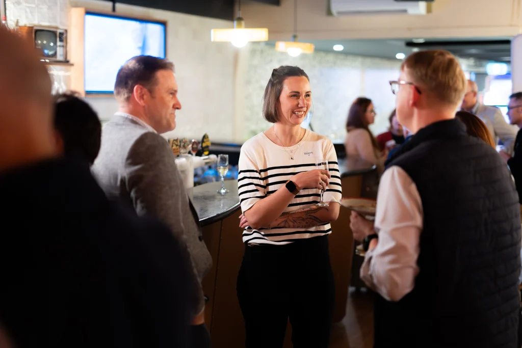 A7403491 1 - TOMRA Cleanaway Smiling woman in a striped shirt holds a glass while chatting with friends at a bar.
