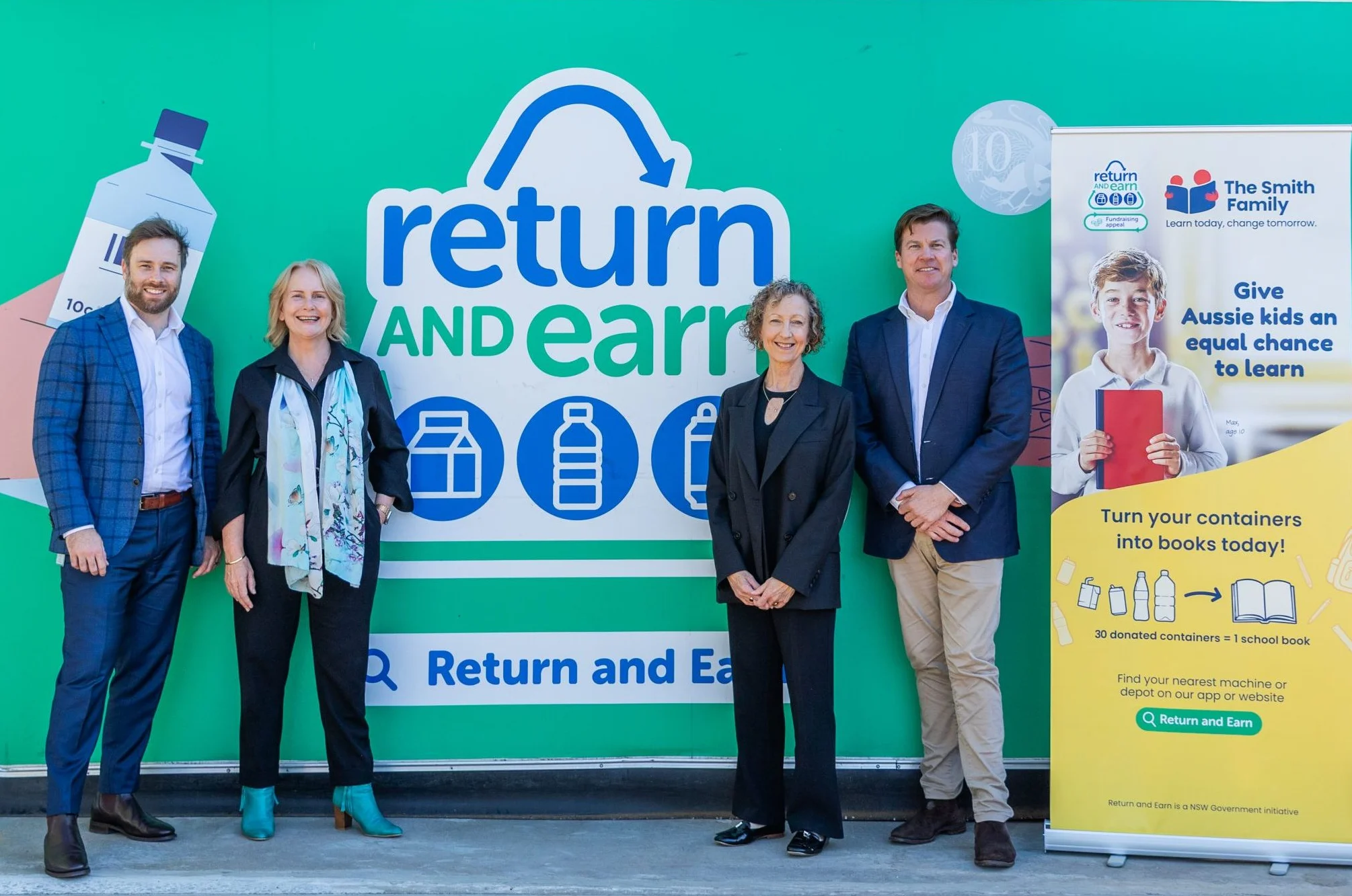 Four people in business attire standing in front of a Return and Earn Machine
