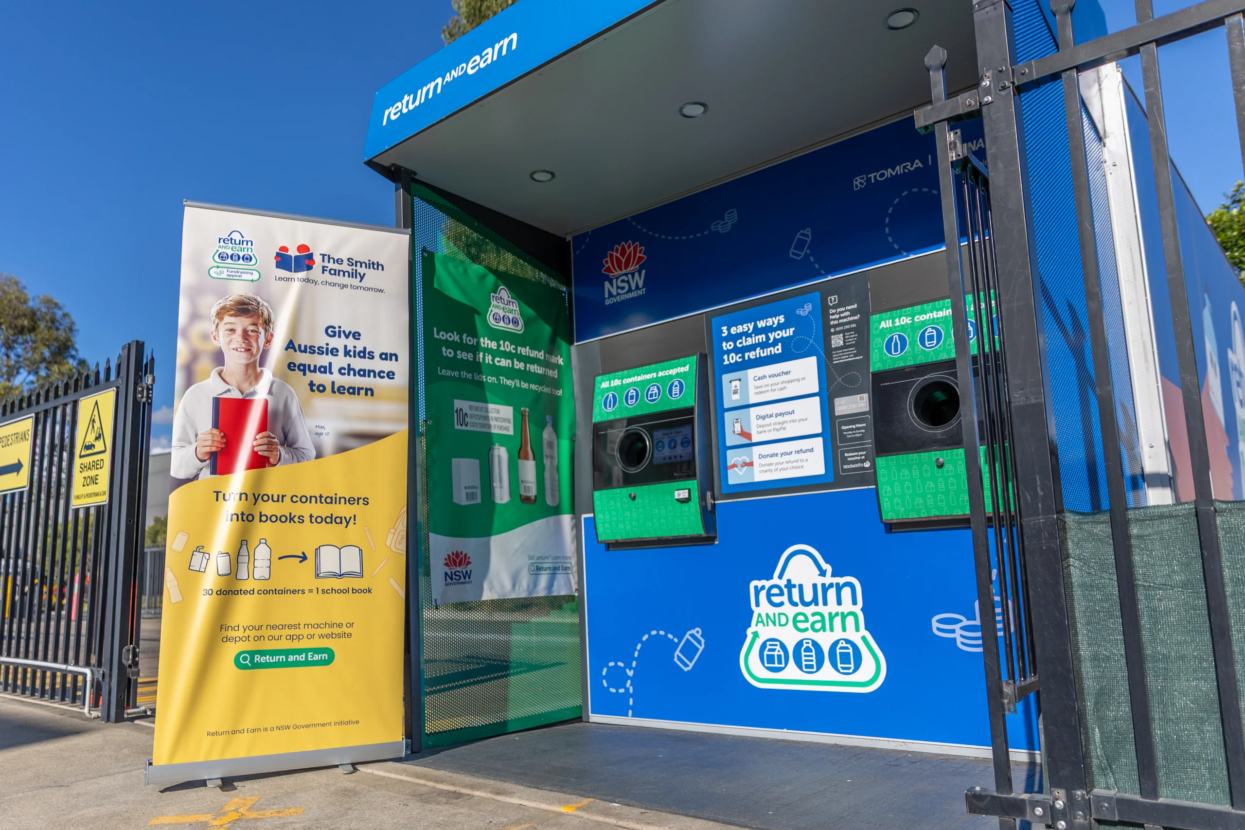 Blue and green Return and Earn Reverse vending machine with a yellow banner from The Smith Family