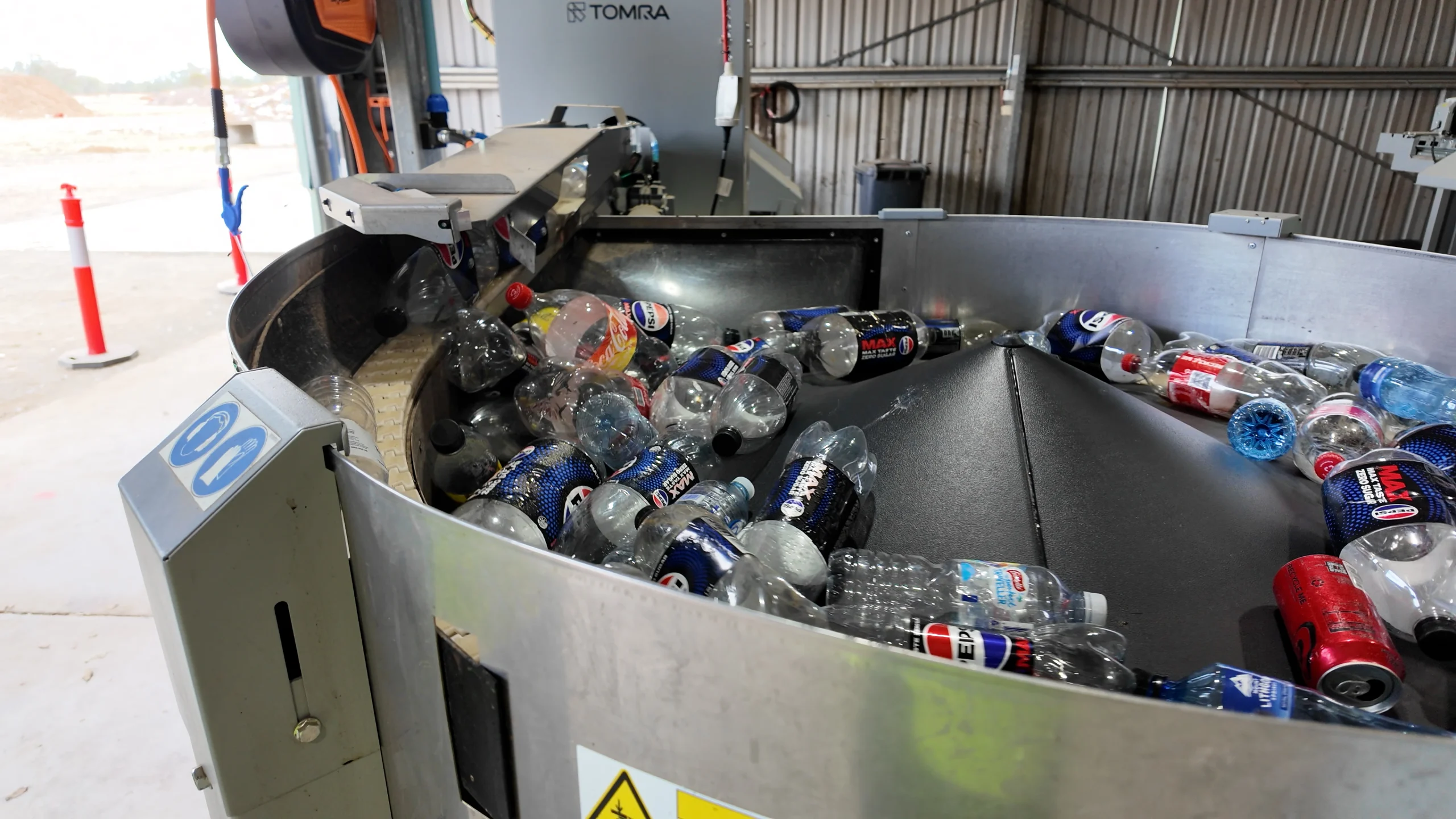 Bulk counting machine at Coonamble Return and Earn Depot - TOMRA Cleanaway Industrial bottle recycling sorter with a conveyor filled with plastic beverage bottles in a warehouse setting, TOMRA machine visible in background.