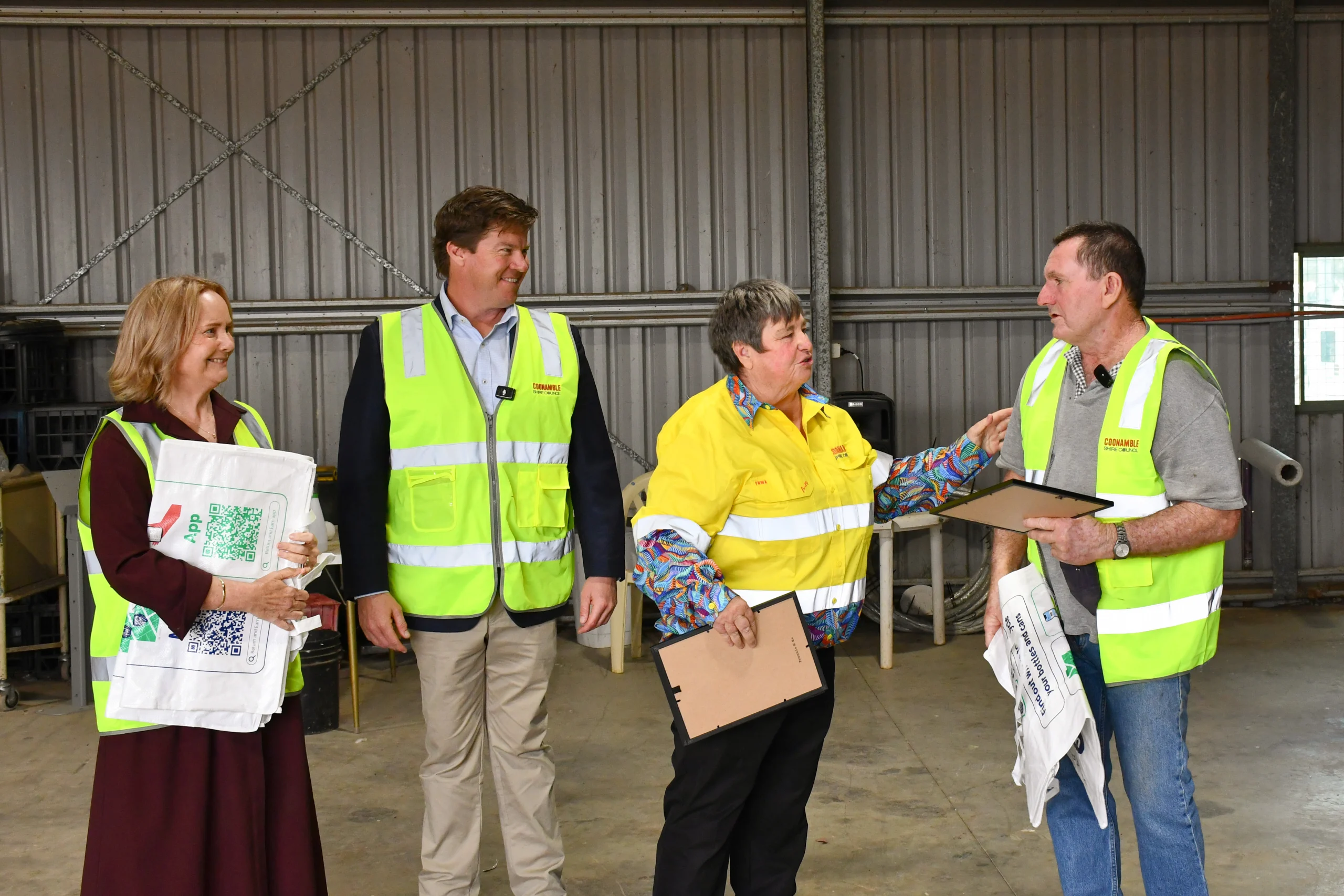 Supercollector for Coonamble Cancer Survivor Fund receiving award at Coonamble Return and Earn Depot opening - TOMRA Cleanaway Four people in high-visibility vests stand in a warehouse, holding clipboards and documents.