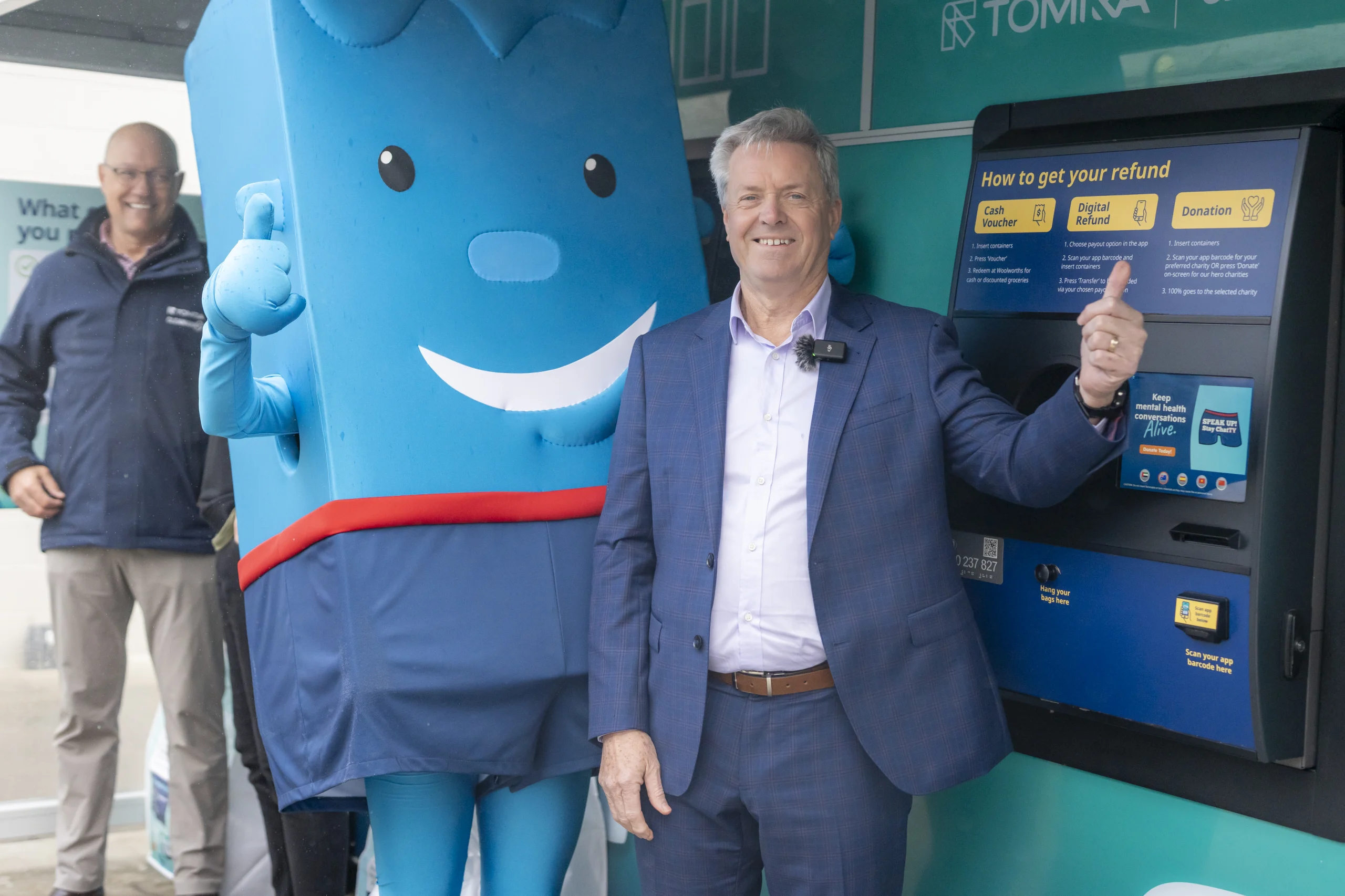 Two men in suits with blue Stay ChatTY mascot with thumbs up standing infront of reverse vending machine